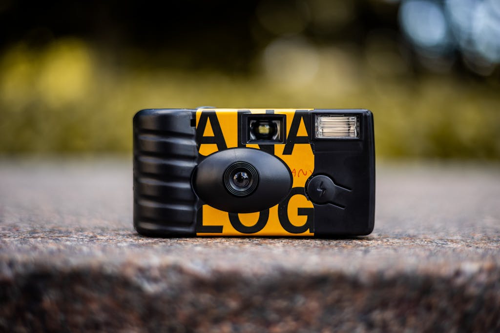 Close-up shot of a stylish disposable camera on a stone surface with blurred natural background.