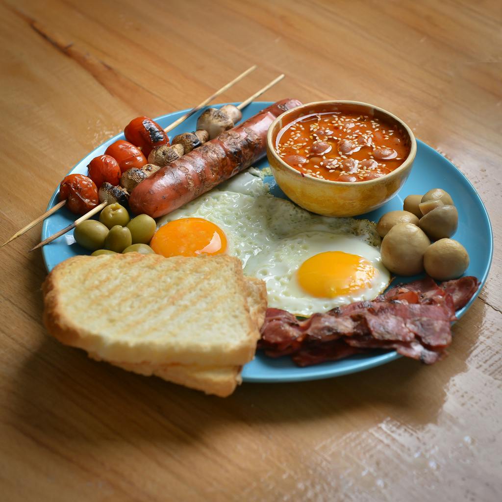 Delicious breakfast platter with fried eggs, sausages, beans, and sides served on a blue plate.