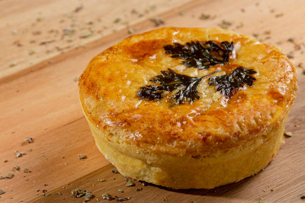 Delicious golden brown savory pie topped with fresh herbs on a wooden background. Perfect for food photography.