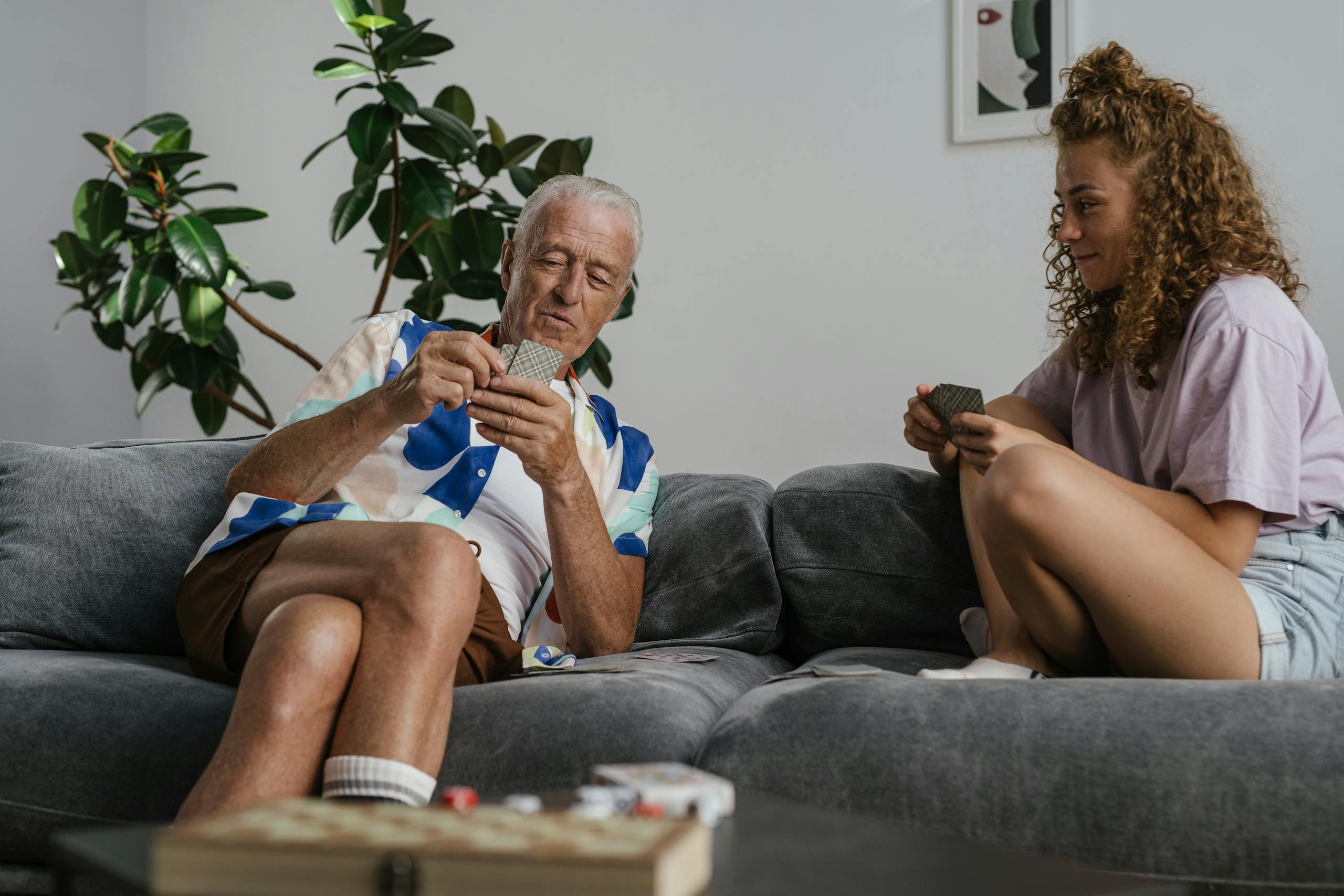 Elderly man and young woman playing cards on a couch, enjoying quality time together.