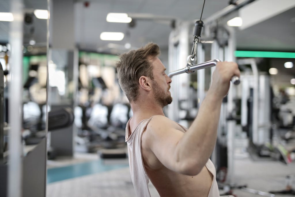 If You Keep Making These 10 Exercise Mistakes, You’ll Never Get Fit 5 Focused man performing lat pulldown exercise indoors.