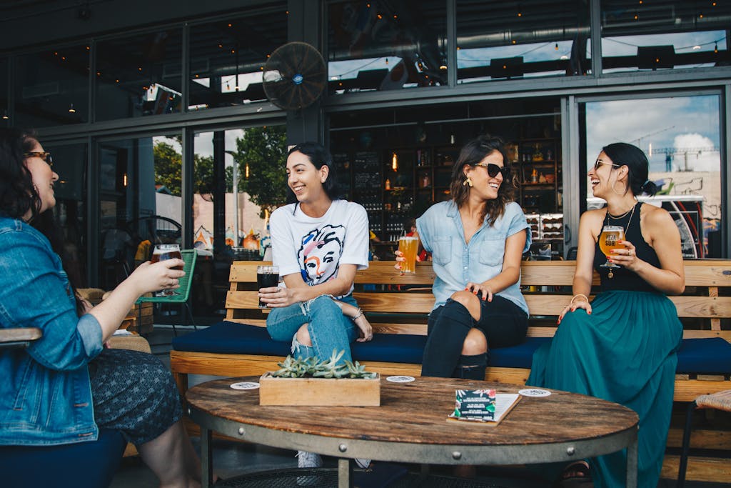 Ignoring These 10 Healthy Habits Could Be Shortening Your Life 2 Four women laughing and having drinks at an outdoor bar, enjoying conversation and friendship.