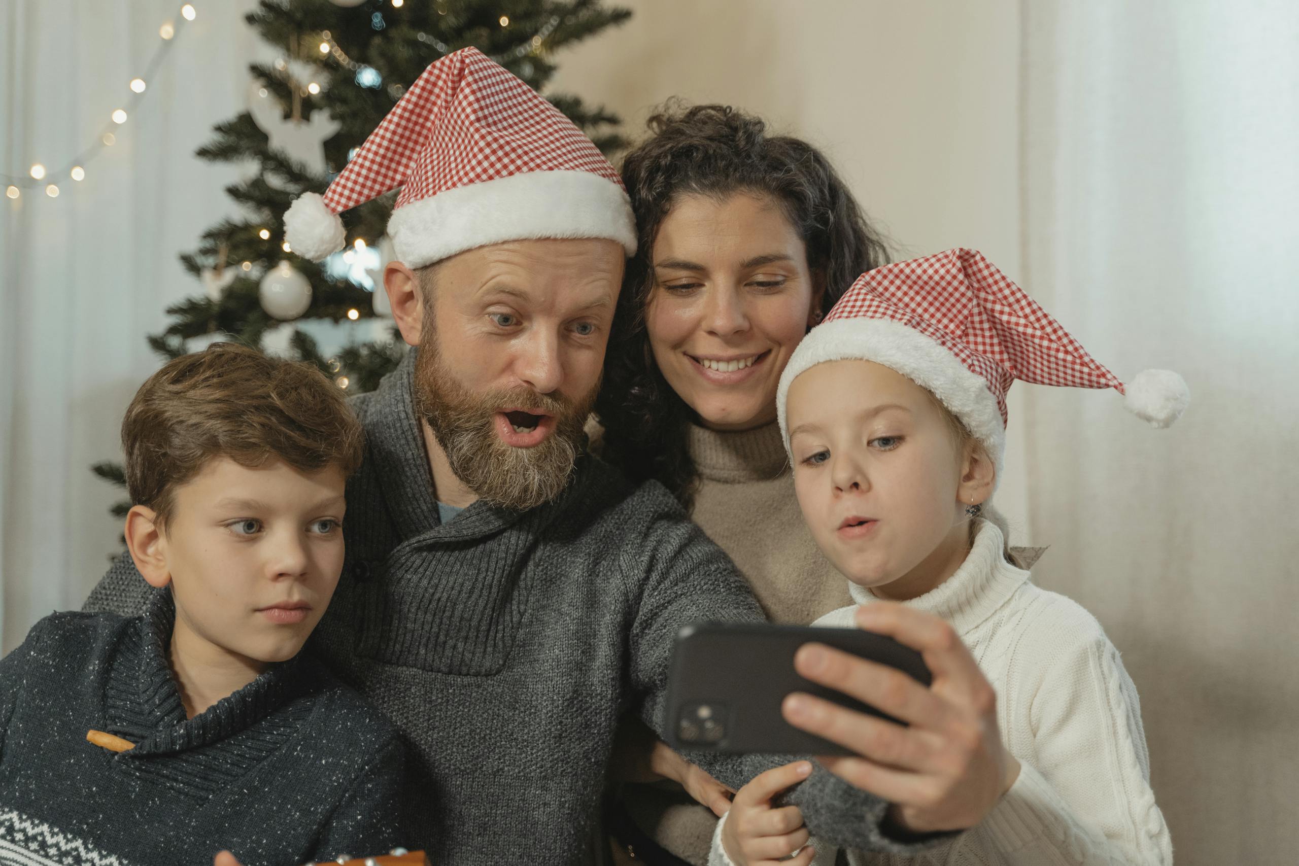 Joyful family wearing Santa hats making a video call at Christmas time, capturing festive togetherness.