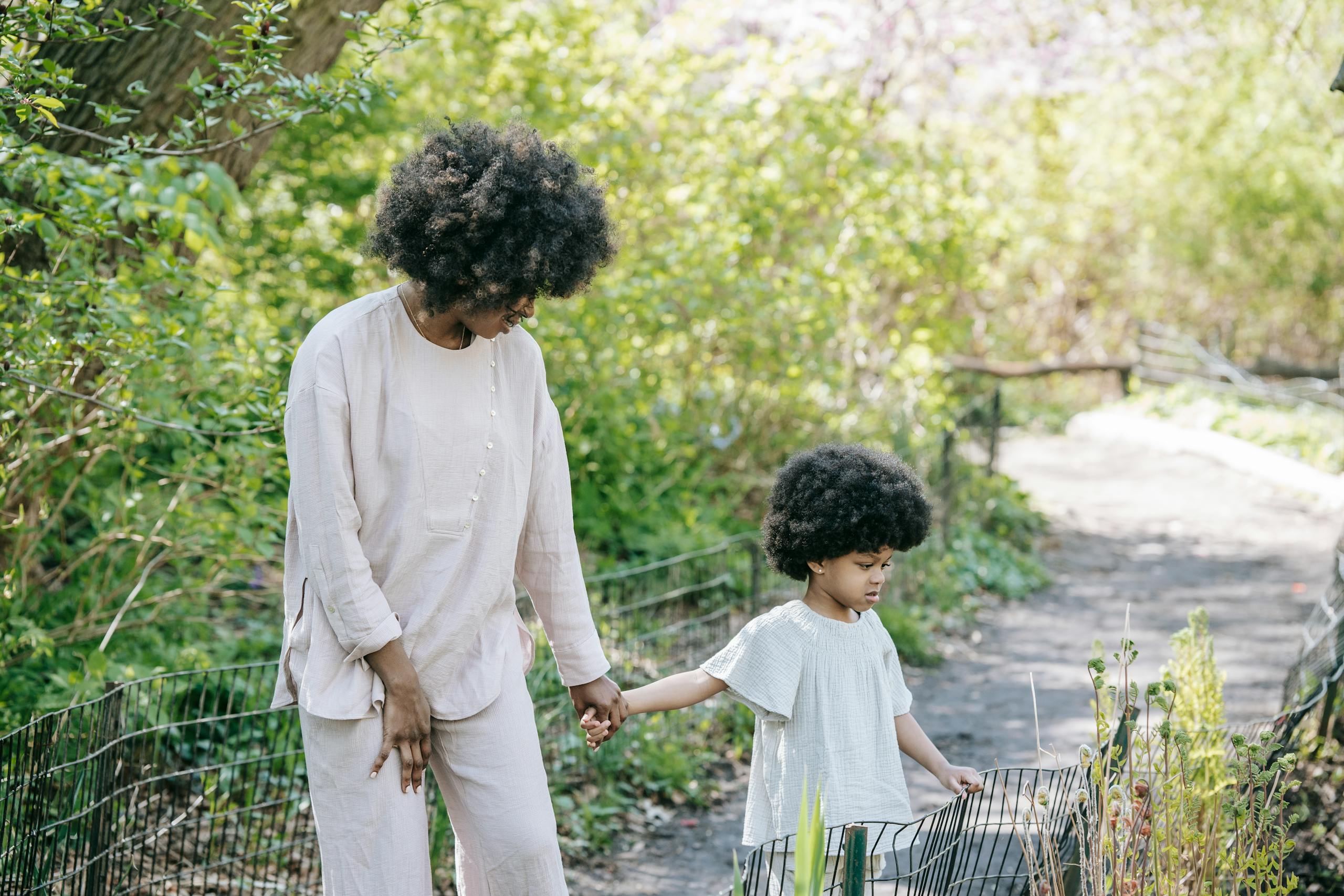 Mother and daughter enjoying a walk in a sunny park, holding hands amidst nature.