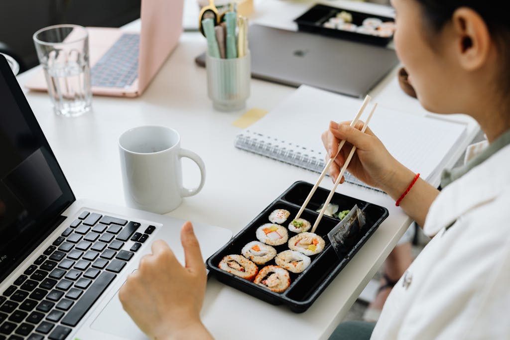 Person having sushi with chopsticks at a desk, blending work and dining.