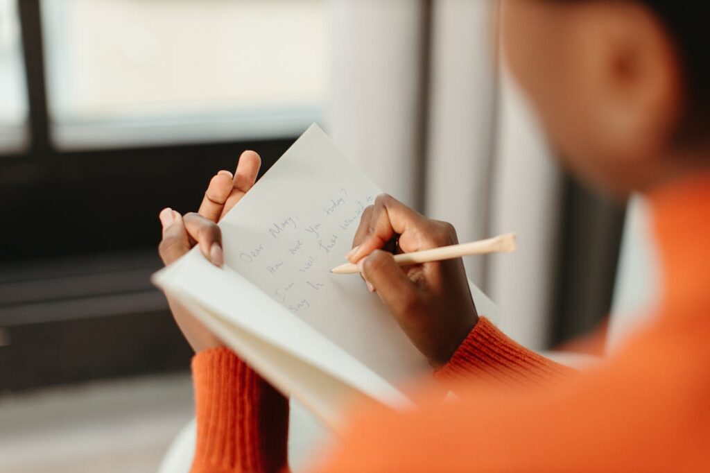 person-in-orange-sweater-writing-a-message-on-a-card-using-pen-