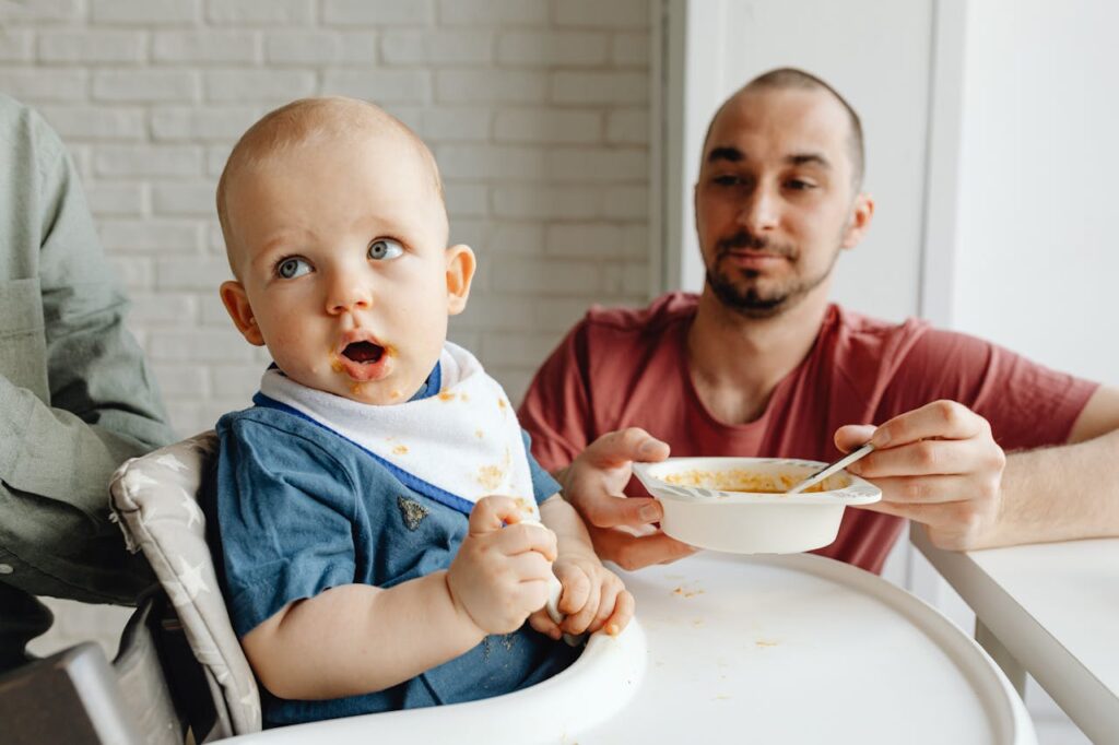 man-in-red-crew-neck-shirt-feeding-a-baby-