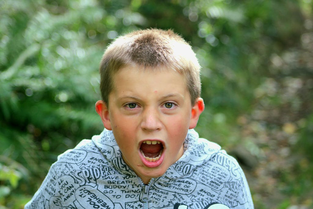 Portrait of a young boy energetically shouting in a lush green outdoor setting.