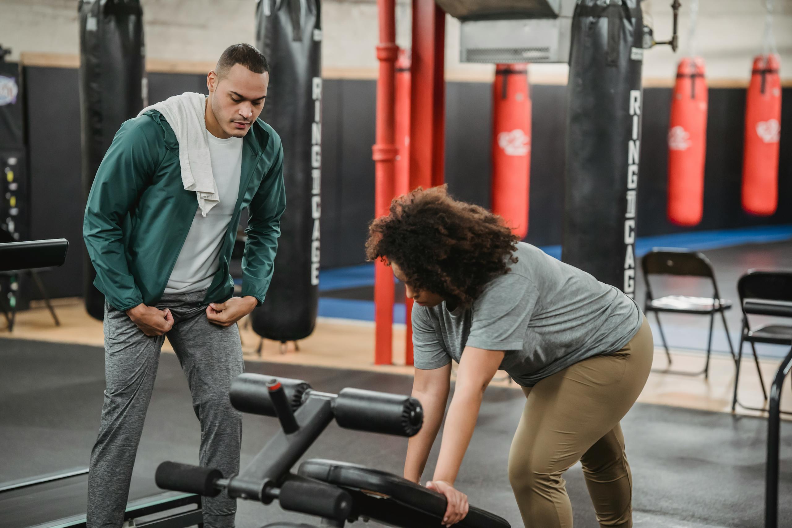 Professional fit instructor helping plus size African American female working out with gym equipment in sport club