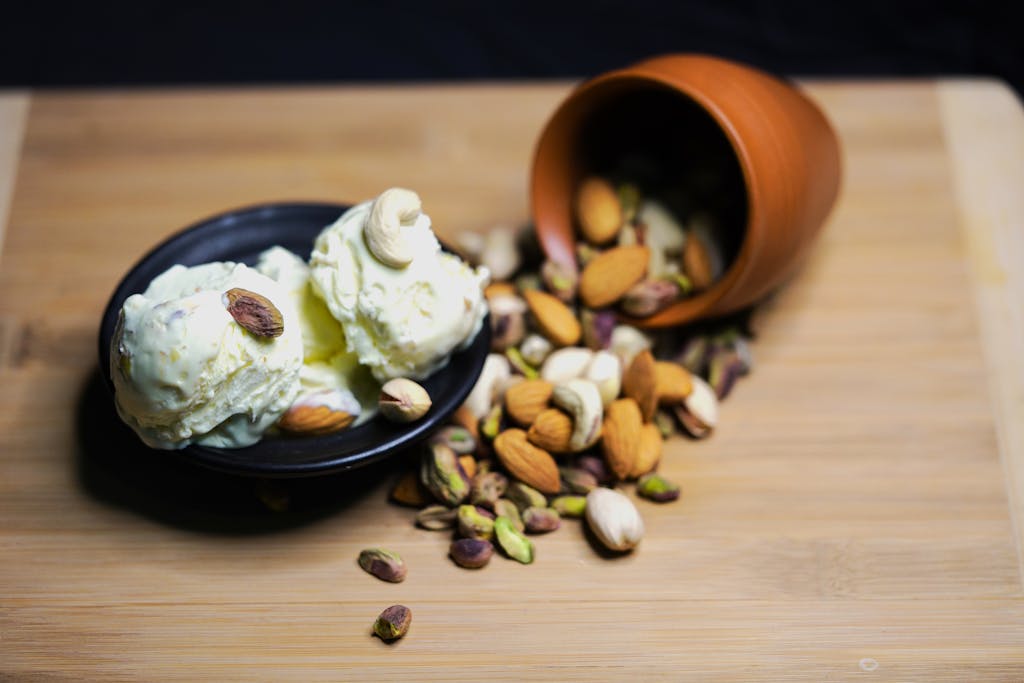 Scoops of ice cream topped with almonds and pistachios, served with mixed nuts on a wooden board.