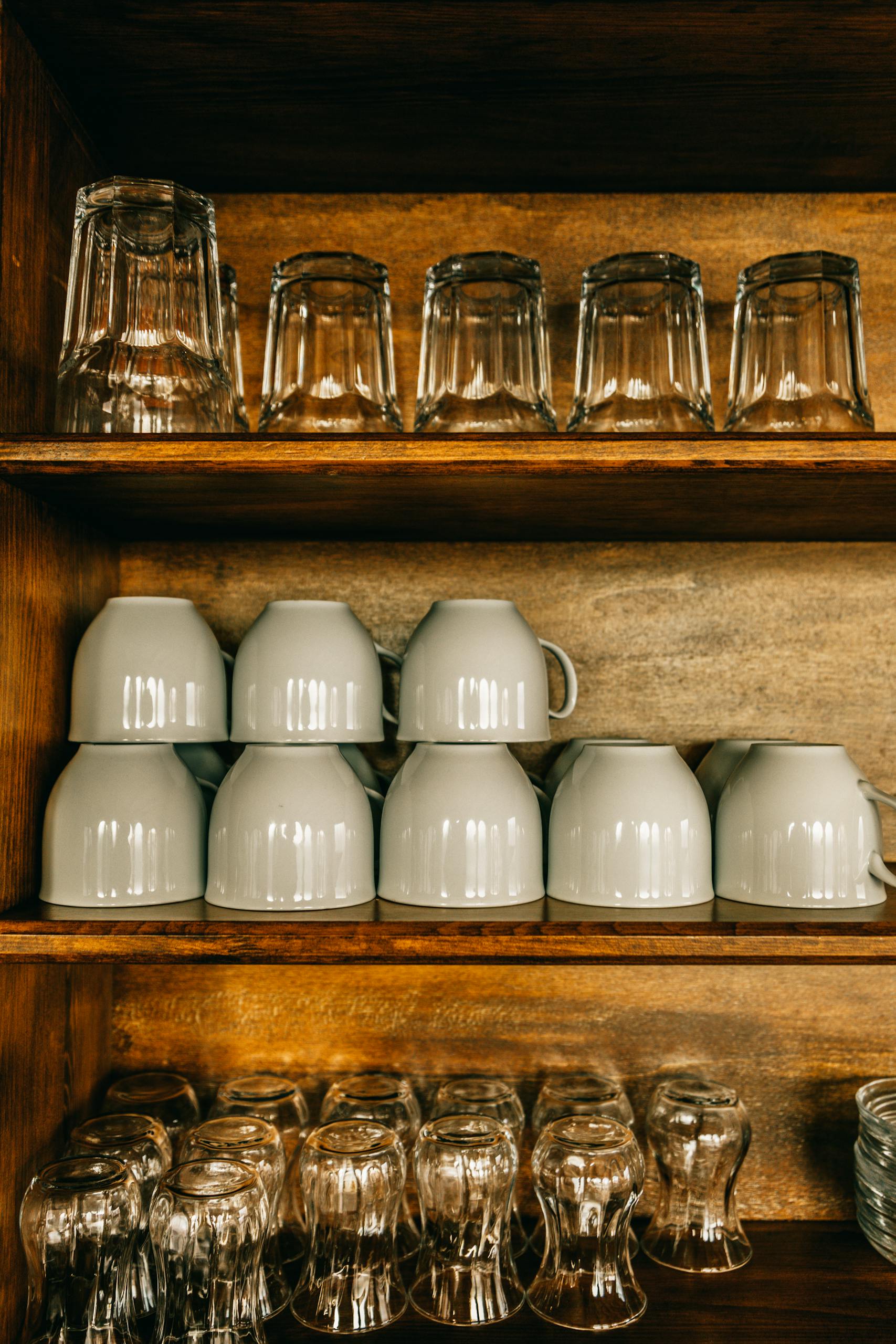Set of assorted cups and glasses placed on wooden shelves in room in daytime