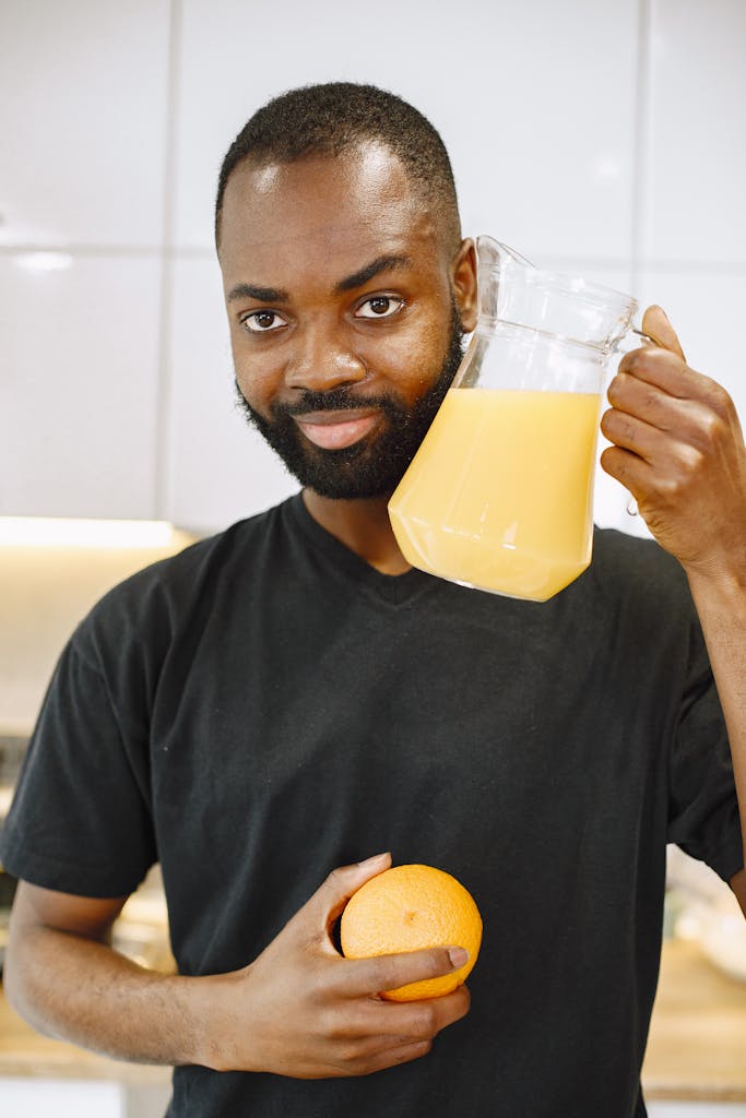 Smiling man holds a pitcher of orange juice and an orange, representing a healthy lifestyle choice.