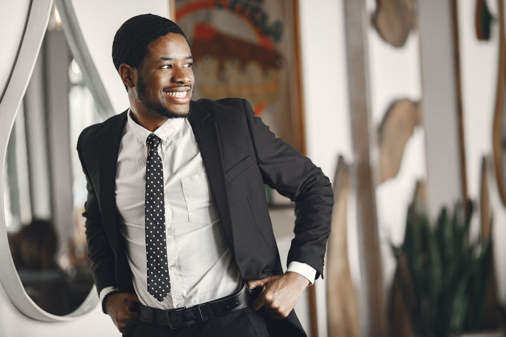 Smiling man in a suit adjusting his belt, exuding confidence in an indoor setting.