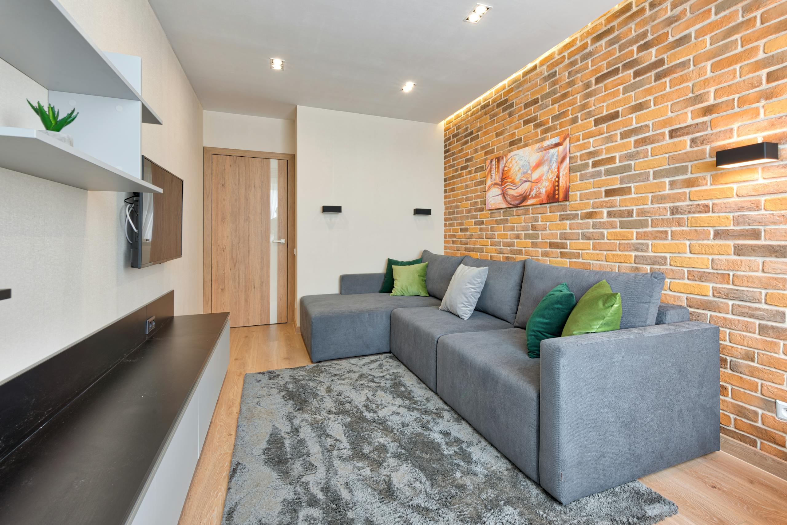 Stylish living room featuring a gray L-shaped sofa, brick wall, and modern decor.