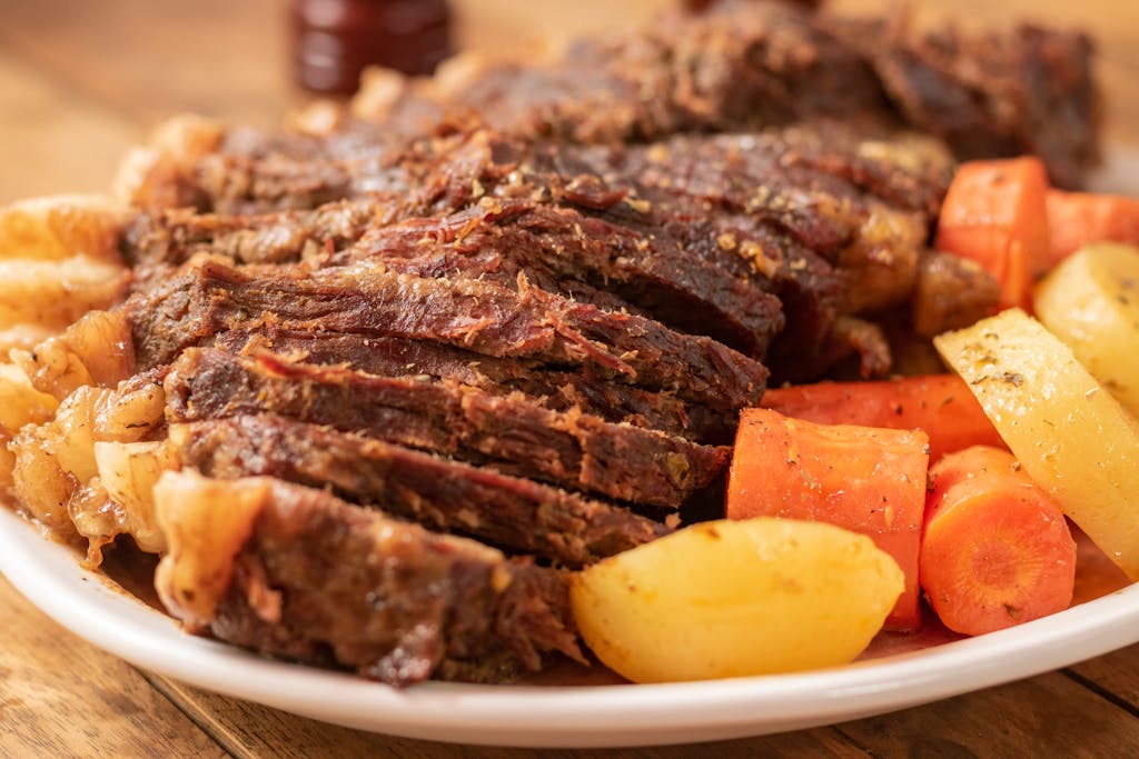 Tender pot roast served with carrots and potatoes on a white plate.