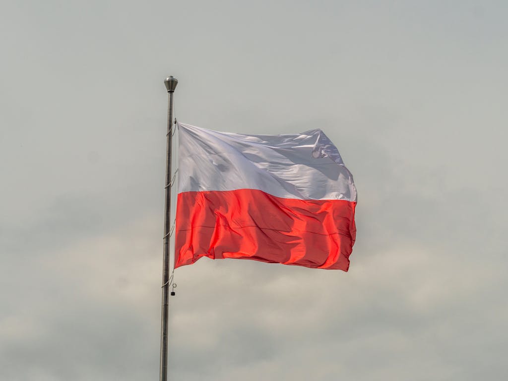 The Polish national flag waving prominently against a cloudy sky, showcasing patriotic pride.