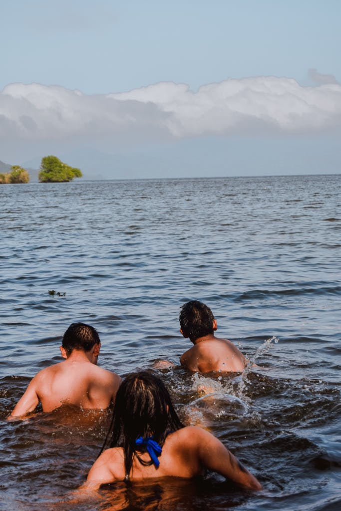 Three children swimming in a tranquil lake under a clear sky.
