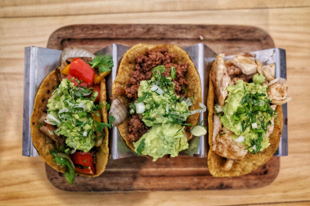 Ignoring These 10 Healthy Habits Could Be Shortening Your Life 3 Three vibrant tacos with fresh guacamole, veggies, and meat on a wooden tray.