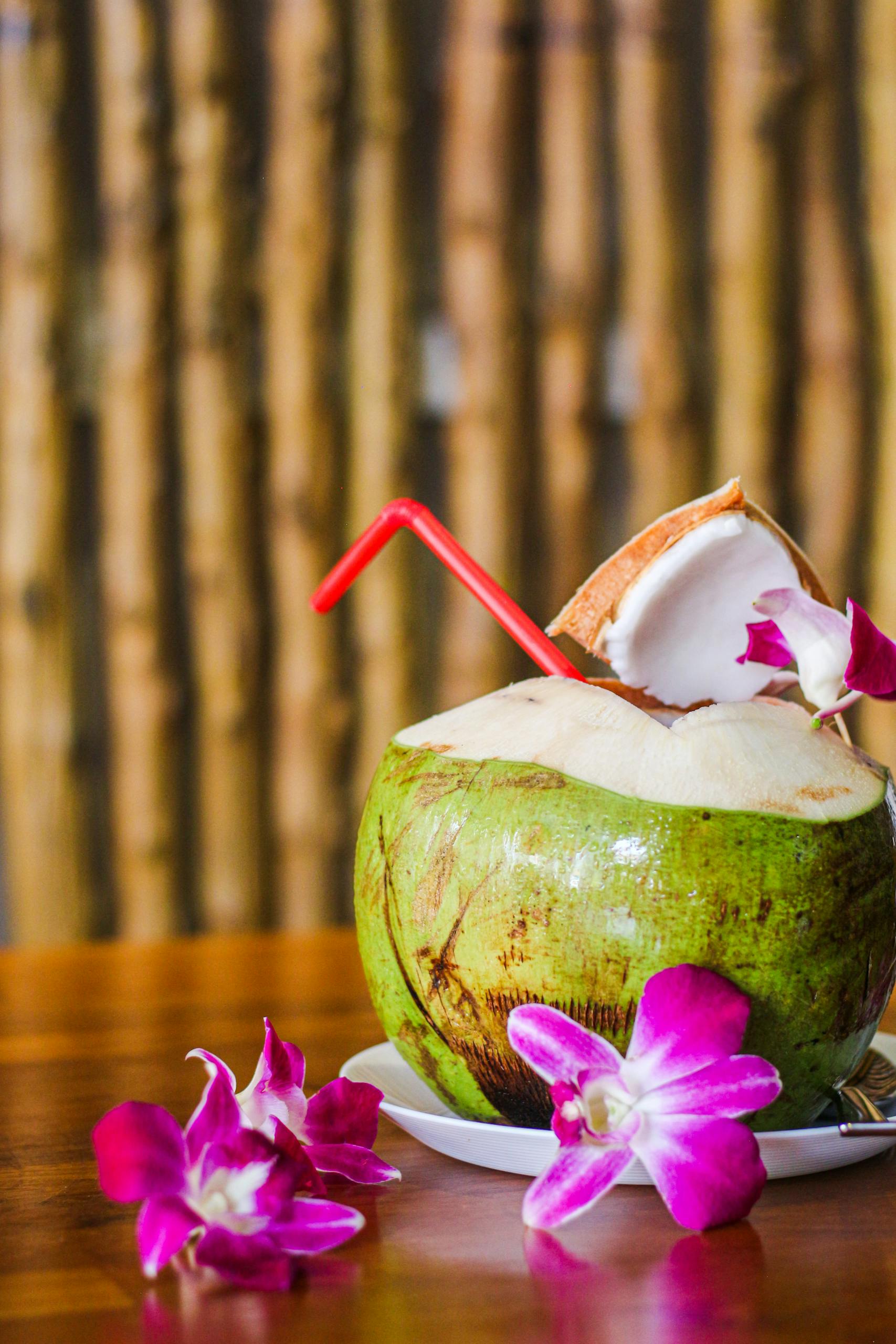 Tropical coconut drink served with pink orchids on a wooden table, perfect for summer vibes.