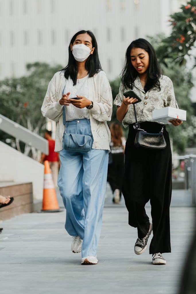 Two women walking in an urban setting, displaying modern fashion and using cellphones.