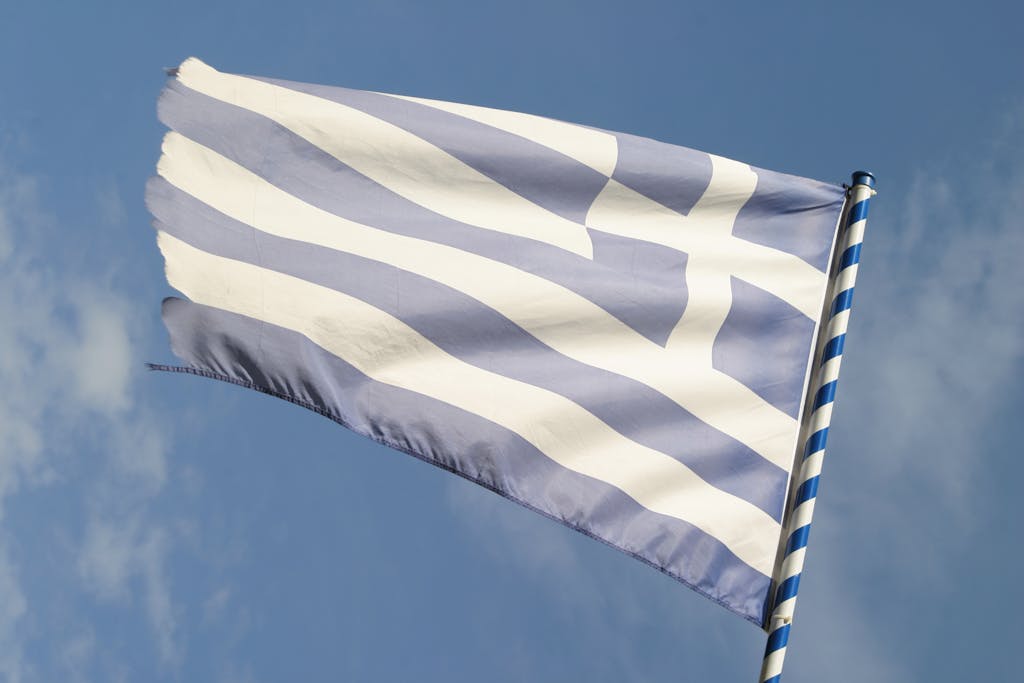 Waving Greek national flag with blue sky background, symbolizing national pride and heritage.