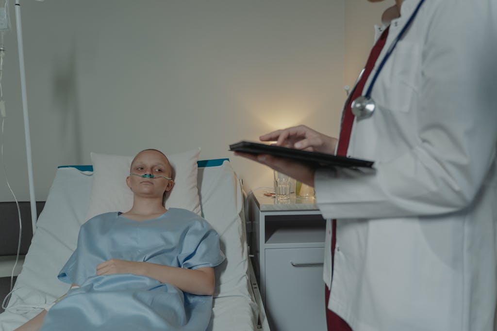 Woman in hospital gown lying in bed, doctor checks digital tablet nearby.