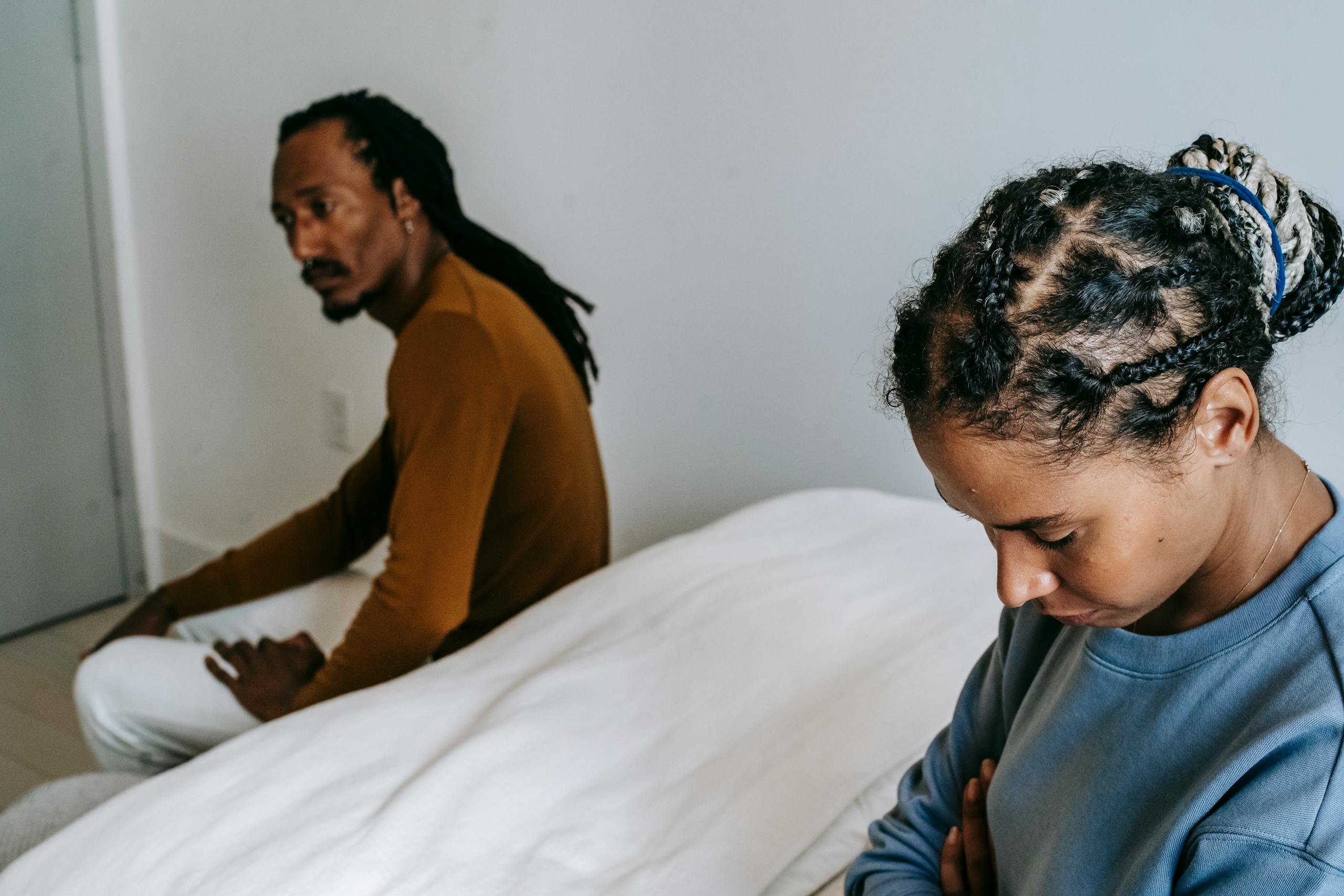 Young black couple in casual outfit sitting on bed with sad face and thinking at home