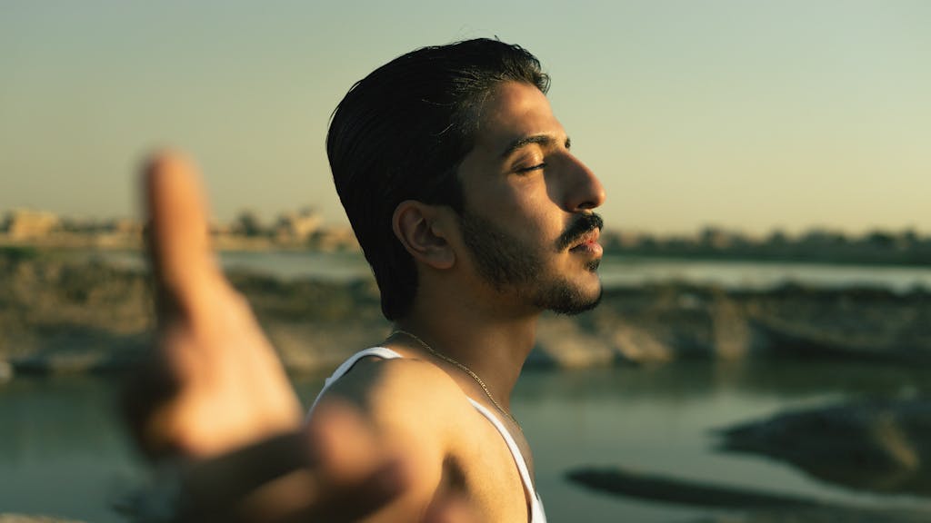 Young man enjoying a tranquil moment by the water, eyes closed in peaceful contemplation.