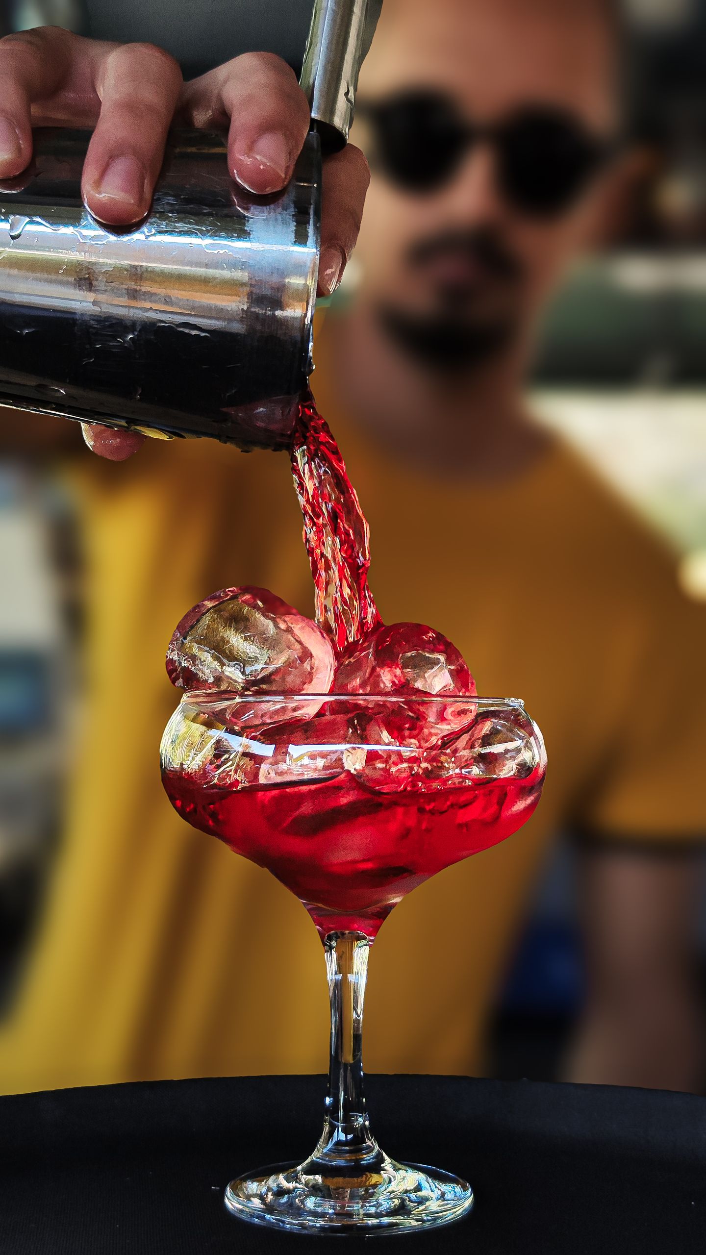 A bartender skillfully pours a vibrant red cocktail into a glass filled with ice.
