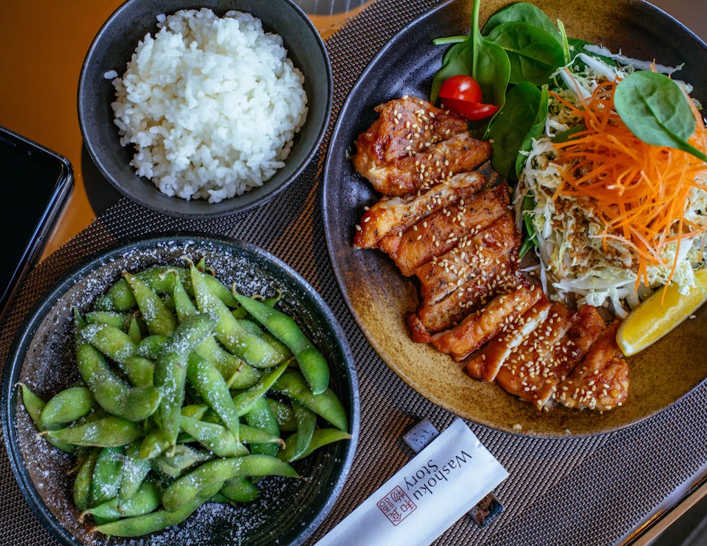 A beautifully presented Japanese meal featuring teriyaki chicken, rice, salad, and edamame.