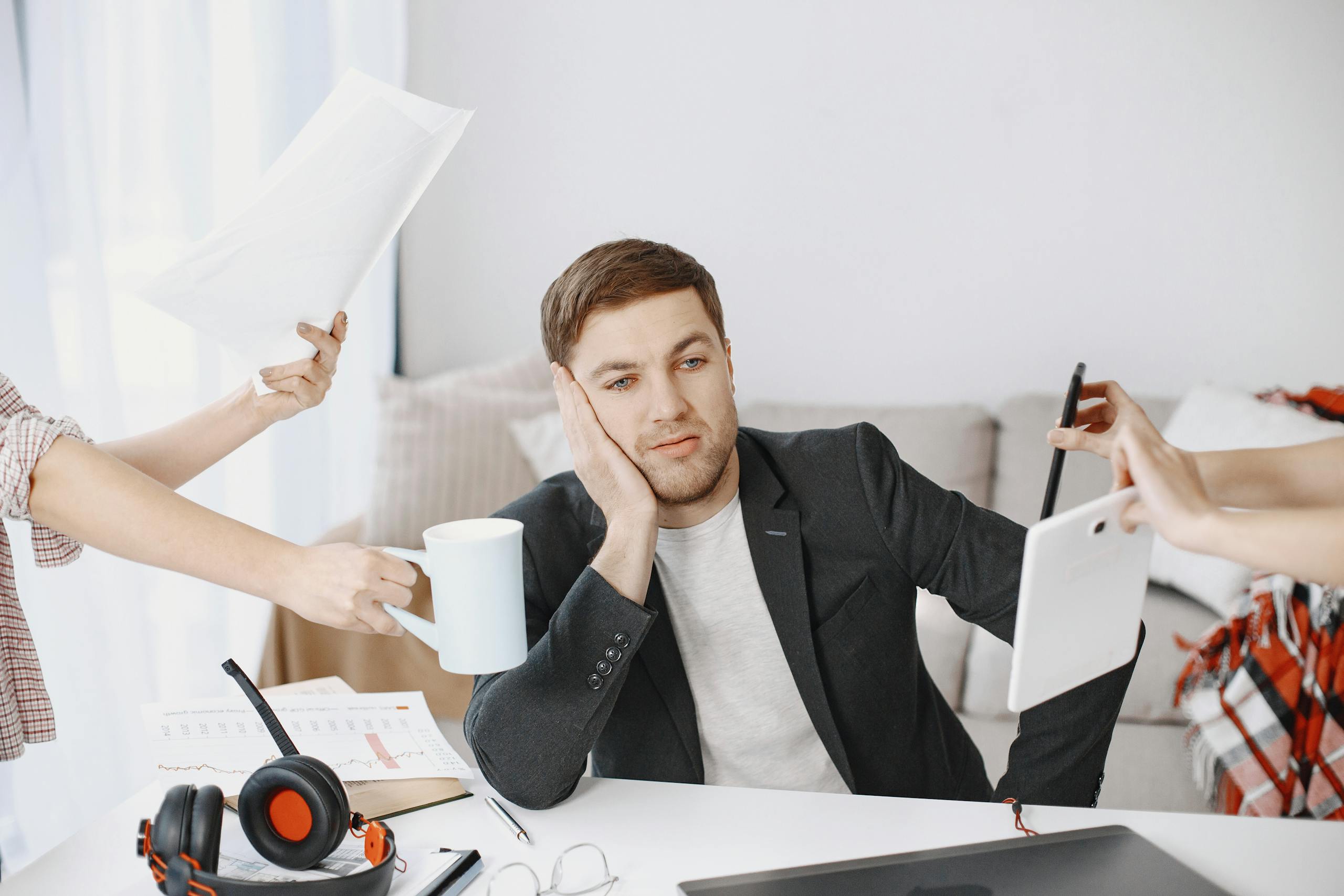 A businessman overwhelmed by tasks in a modern office setting, depicting multitasking and stress.