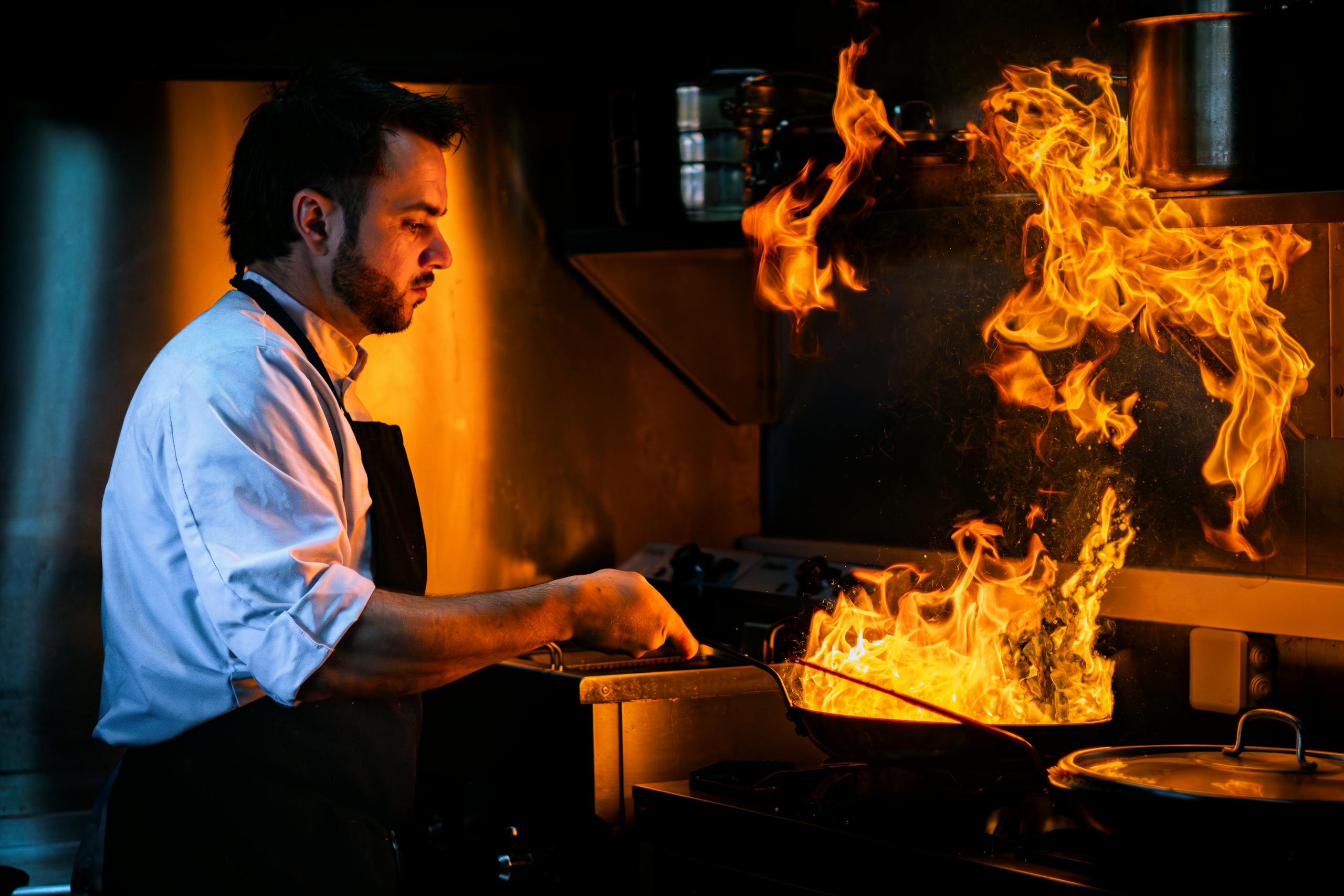 A chef skillfully prepares a dish with a dramatic flame in a modern kitchen setting.