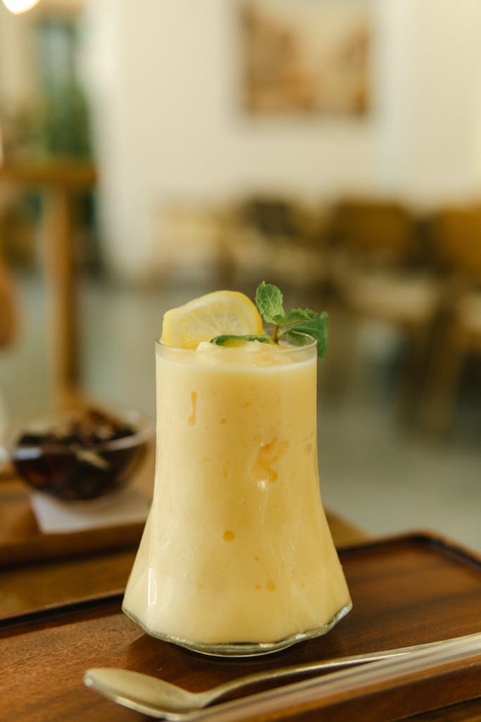 A chilled lemon smoothie with mint garnish served on a wooden tray in a cozy cafe setting.