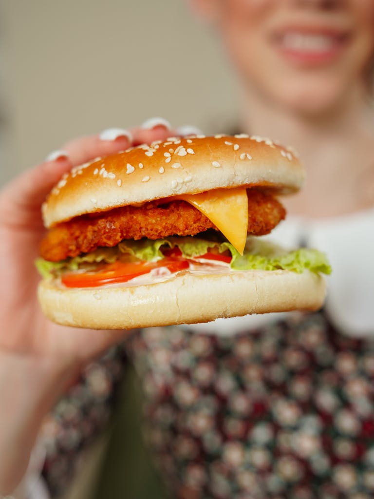 A close-up of a woman holding a delicious chicken burger with lettuce, tomato, and cheese.