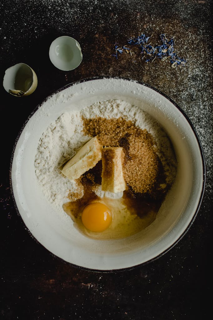 A close-up of baking ingredients including flour, sugar, butter, and egg in a bowl, ready to mix.