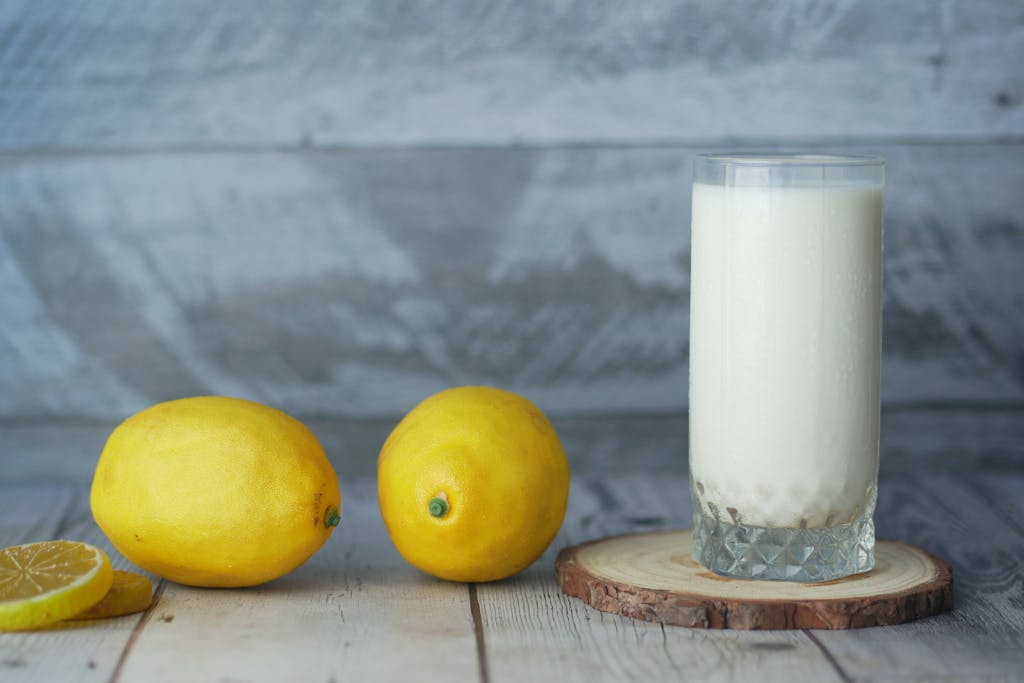 A close-up of fresh lemons and a glass of milk on a wooden table.