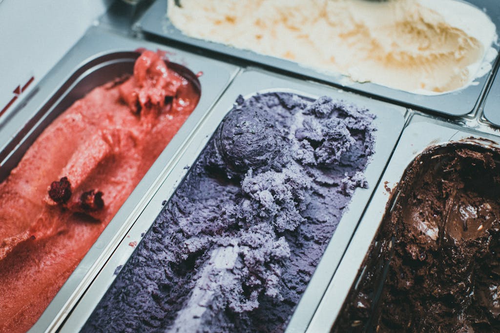 A close-up view of various flavored ice cream in metal trays, showcasing vibrant colors and textures.