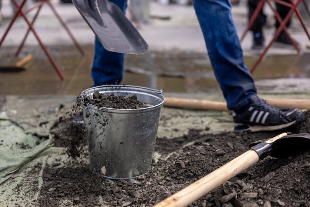 A construction worker shoveling soil into a bucket during a workday outdoors.