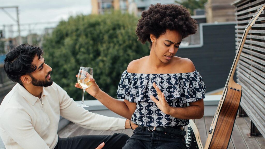A couple experiencing a tense moment during a rooftop picnic with wine, roses, and a guitar. Urban setting.