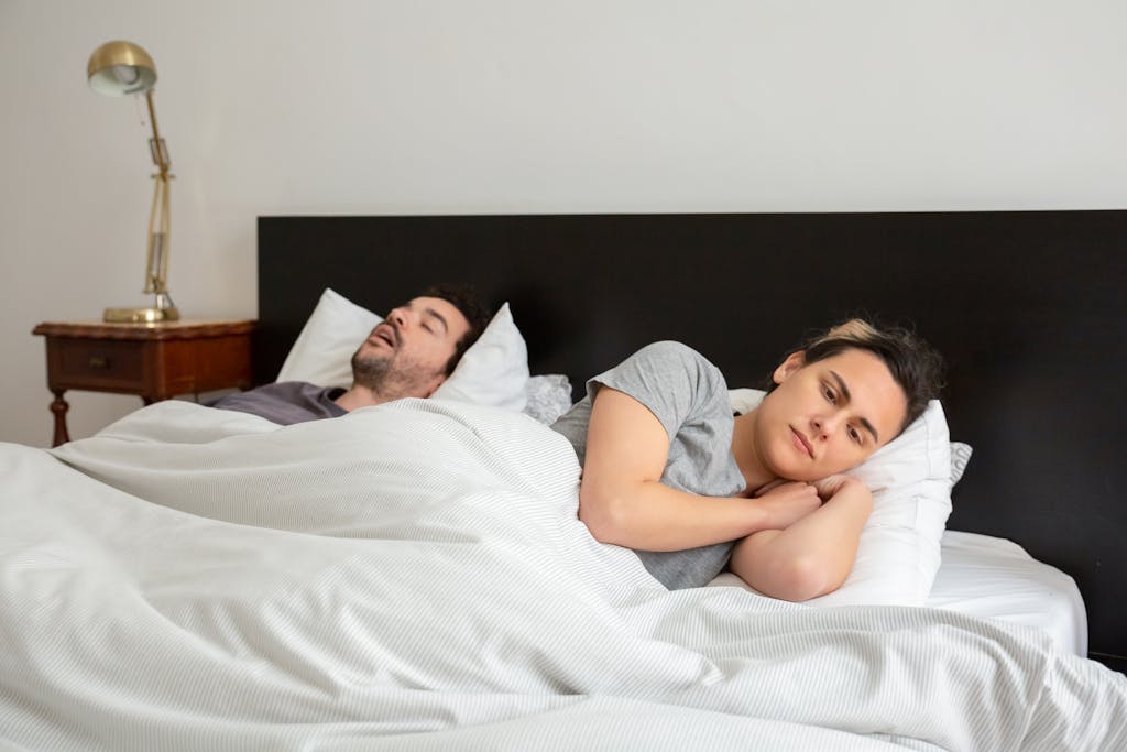 A couple in bed, one person lying awake as the other snores peacefully.