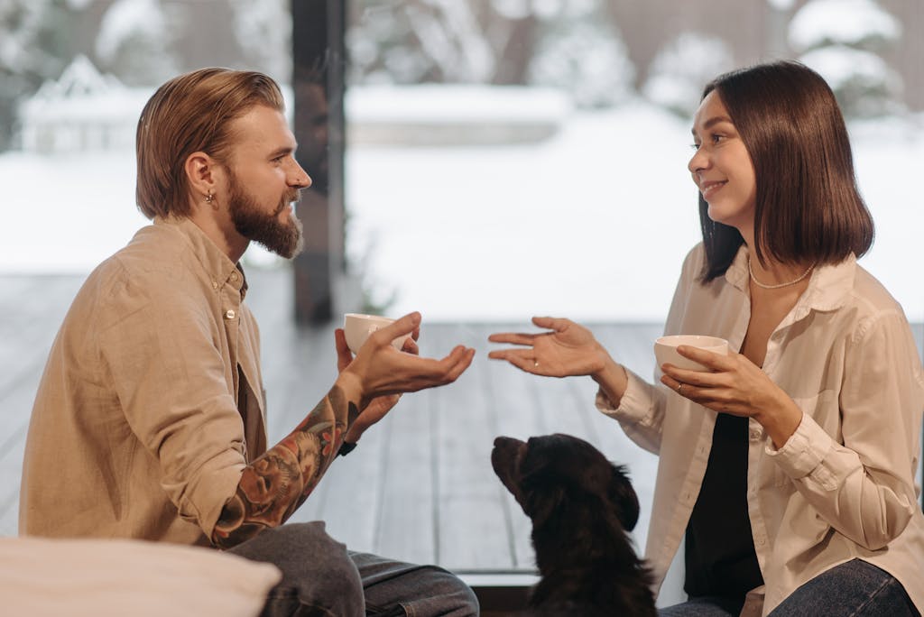 A couple with a dog enjoying coffee indoors by the window in winter.