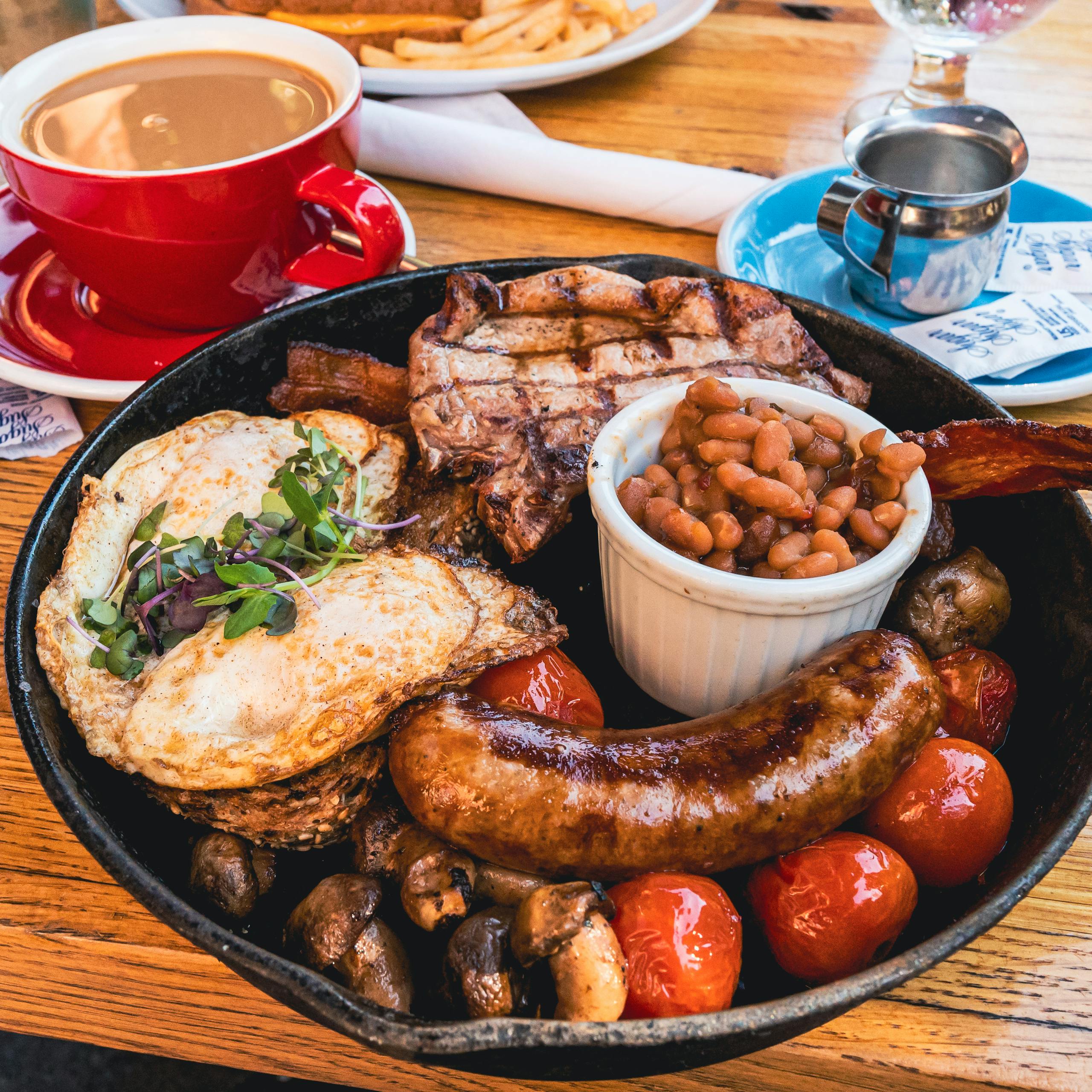 A delicious traditional English breakfast featuring eggs, sausage, bacon, beans, and coffee served indoors.
