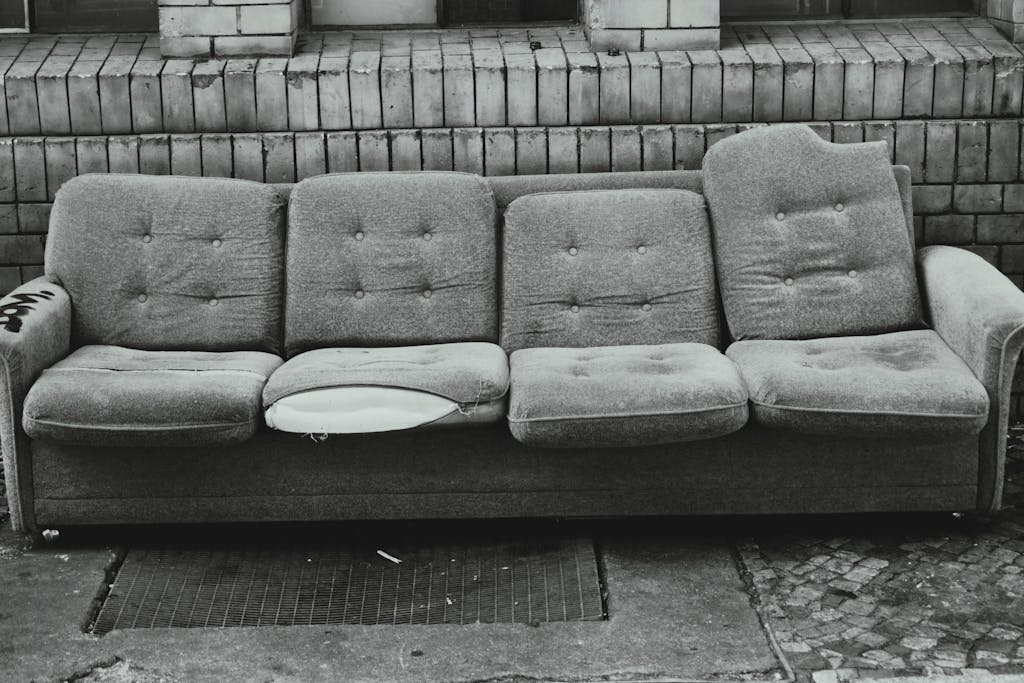 A grayscale image of an abandoned torn sofa against a brick wall in Berlin.