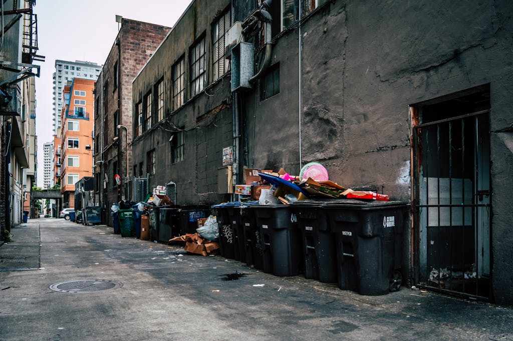 A gritty urban alley in Seattle with overflowing trash bins and high-rise buildings.