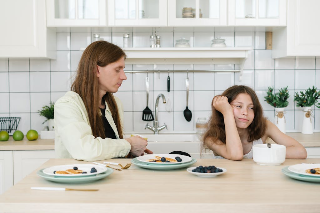 A man and girl sitting at a kitchen table with breakfast bowls and plates on a calm morning.