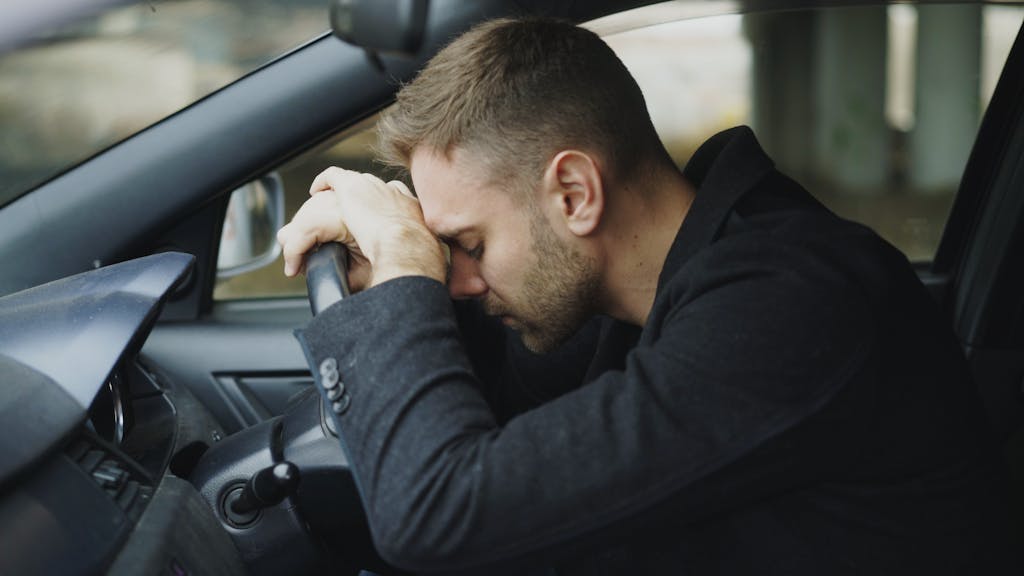 A man showing stress while sitting in a car, head on steering wheel.