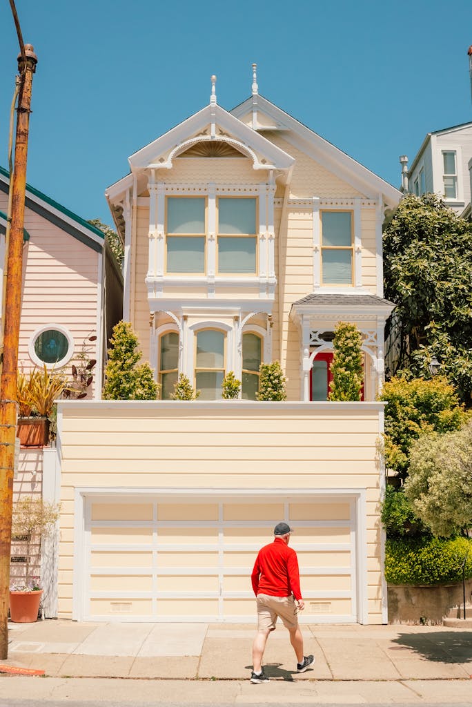 A man walks by a sunlit Victorian house in an urban neighborhood.