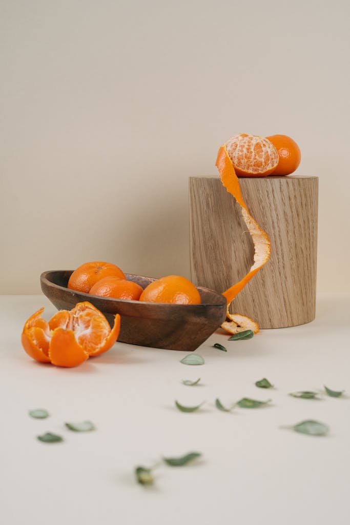 A minimalist still life of vibrant tangerines with leaves, artfully arranged on wooden surfaces.