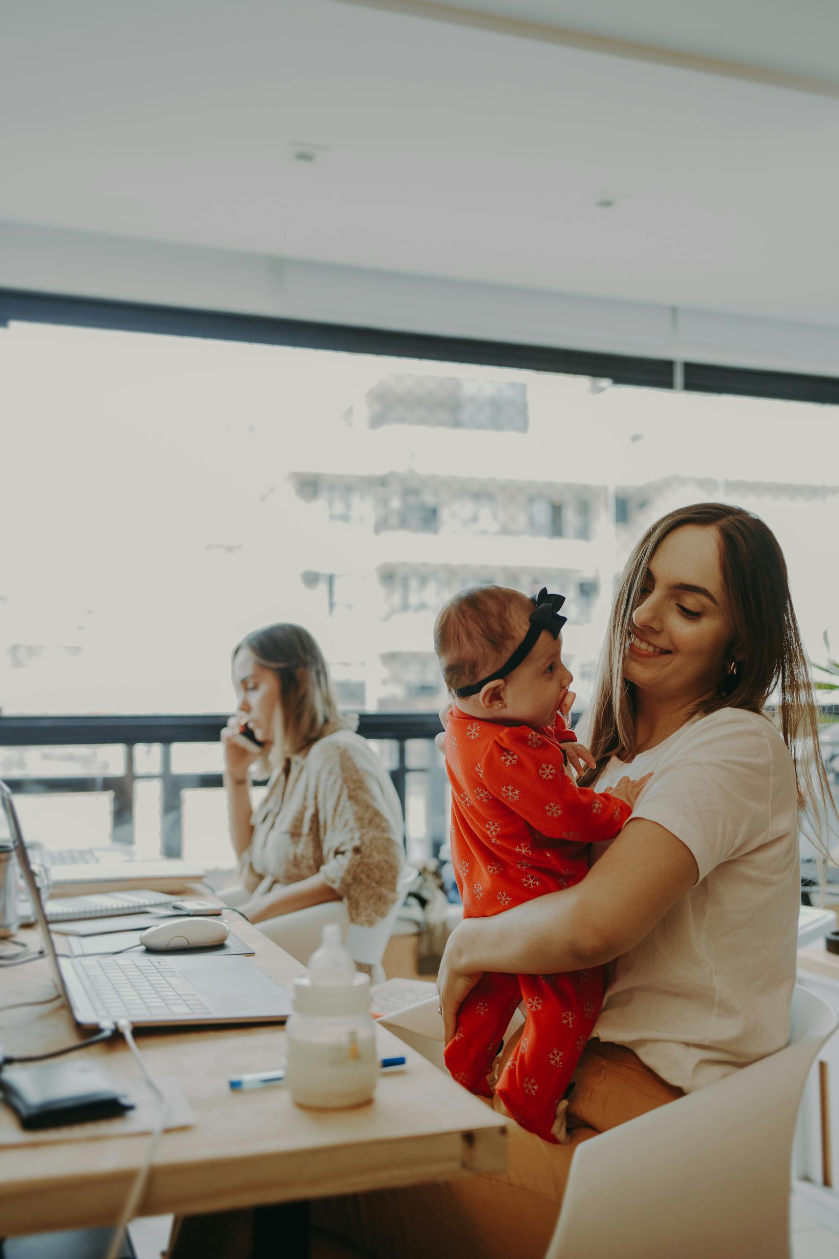 A mother holding her baby while working at a modern office, exemplifying work-life balance.