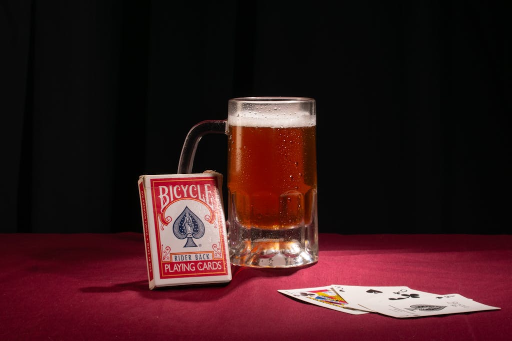 A mug of beer beside a deck and spread of playing cards on a red table.